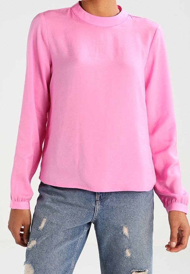 Blusa rosa a maniche lunghe con scollo a girocollo, realizzata in tessuto morbido. Presenta polsini elasticizzati e una vestibilità comoda, abbinata a jeans blu strappati.