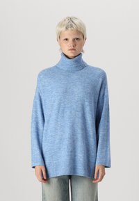 Pull à col roulé oversize bleu clair en tricot doux et texturé avec des accents ribbed au niveau du col et des poignets. Manches longues, coupe décontractée.