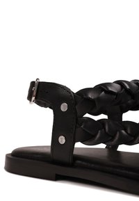 Κοντινή λήψη μαύρης σάνδαλας με πλεκτούς δερμάτινους ιμάντες, επίπεδη σόλα και ρυθμιζόμενο κούμπωμα με αγκράφα σε λευκό φόντο.