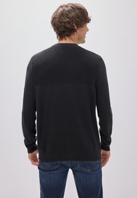 Schwarzer Pullover mit langen Ärmeln und einem strukturierten Rippenmuster über dem oberen Rücken. Weicher Stoff und elastische Bündchen, kombiniert mit Jeans.