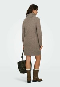 Preveliki taupe pleteni džemper haljina s visokim ovratnikom, rebrastim manžetama i rubom. Model ga kombinira s torbom s uzorkom leopard i smešnim čizmama do koljena.