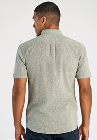 Korteklevige, geblokte blouse in lichtgroen, met een textuur, voorzien van een middenachter plooien en gladde randen aan de zoom.