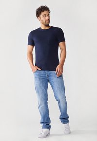 Marineblå, kortermet t-skjorte med strukturert stoff og lomme, kombinert med lys blå jeans og hvite sneakers.