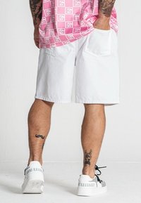 Shorts bianchi in cotone con una vestibilità ampia, tasche posteriori e orlo piatto, abbinati a sneakers bianche con dettagli del logo.