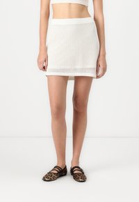 White knit mini skirt with a textured pattern, elastic waistband, and straight cut. Paired with brown leopard print flats.
