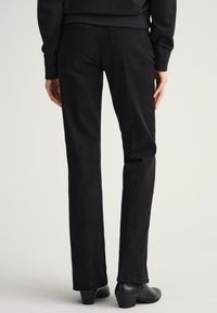 Jeans rectos negros hechos de algodón, con bolsillos estándar, una textura suave y un diseño sencillo, combinados con botas de tacón negras.