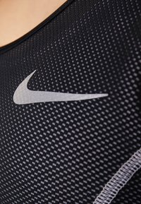 Débardeur de sport noir avec un motif texturé à pois. Présente un logo Nike réfléchissant en argent à l'avant.