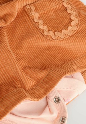 Kardoray-baby jumpsuit i bränd orange med vågig ficktrim, med tryckknappsstängning och ljusrosa foder med blommönster.