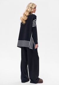 Czarny i biały sweter w paski, wykonany na drutach, o luźnym kroju, z bocznymi rozcięciami i długimi rękawami, zestawiony z szerokimi czarnymi spodniami.