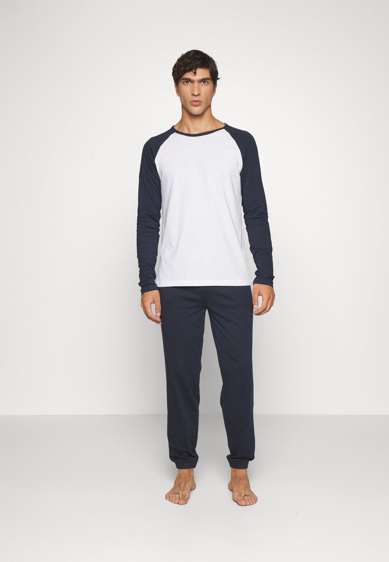 Heren loungewear set bestaande uit een wit en marineblauw raglan t-shirt met lange mouwen en marineblauwe broek, beide gemaakt van zachte, lichte stof.