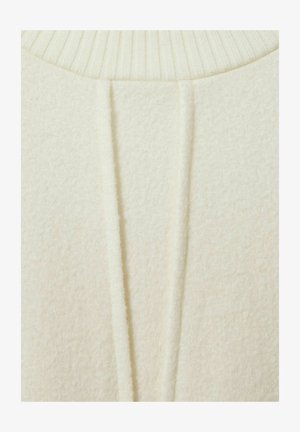 Tricoul de culoare crem are o textură moale, cu o suprafață texturată și detalii ribbate la gât, precum și o cusătură centrală.