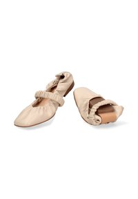 Ballerine di pelle morbida beige con fasce elastiche, una scarpa piegata per mostrare la flessibilità e suole piatte marroni.