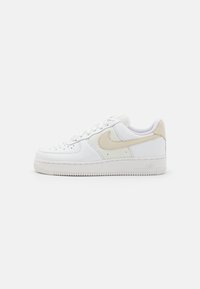 Låg vit sneaker med beige Nike-swoosh och meshpaneler, perforerad tå, snörningsstängning och tjock gummisula.
