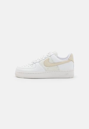 Baskets blanches basses avec un swoosh beige de Nike et panneaux en mesh, bout perforé, fermeture à lacets et semelle en caoutchouc épaisse.