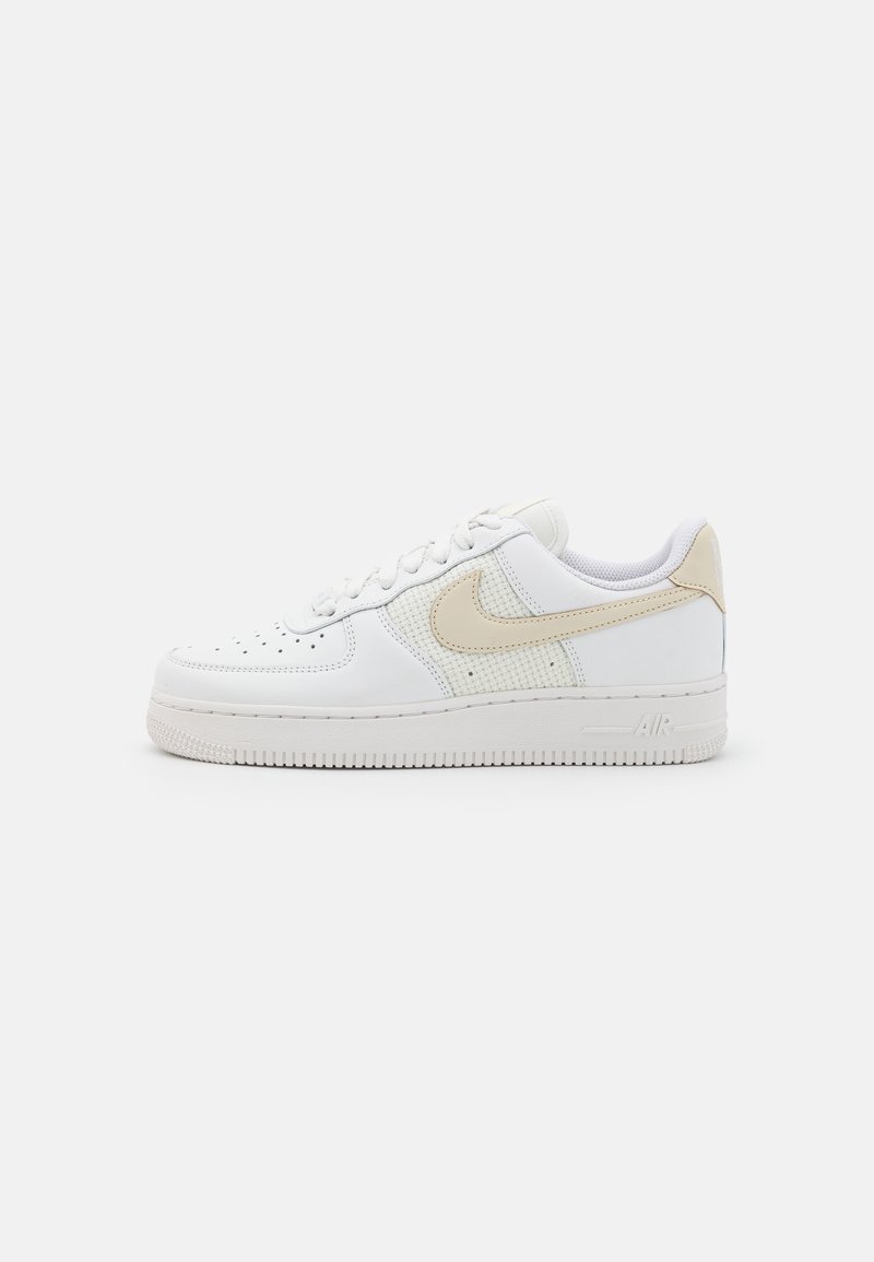 Låg vit sneaker med beige Nike-swoosh och meshpaneler, perforerad tå, snörningsstängning och tjock gummisula.