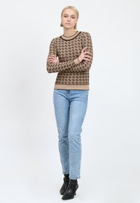 Maglione a maniche lunghe marrone con motivo, design aderente, scollo rotondo e polsini a costine, abbinato a jeans azzurri chiari e stivali neri alla caviglia.