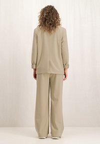 Beige relax-fit pak met een langmouwen jasje en brede broekspijpen, gemaakt van zachte stof met een gladde textuur en minimale stikdetails.