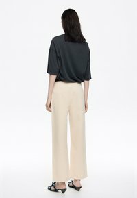 Camiseta oscura de gran tamaño, pantalones crema de corte holgado y sandalias de tacón negras con lazos decorativos, vistas desde atrás.
