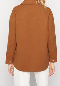 Brun ulljacka med krage, långa ärmar och tryckknappsmuddar. Har en mjuk textur och en något rundad nederkant.