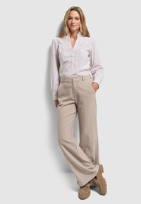 Lekko w prążki bluzka z długim rękawem i kołnierzykiem w odcieniach kości słoniowej i beżu. Beżowe szerokie spodnie w neutralnym kolorze, zestawione z brązowymi butami na platformie.