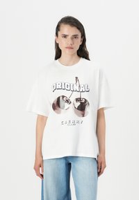 Balta per didelį t-shirt'ą, kuriame pavaizduotos vyšnios ir užrašas "ORIGINAL CHERRY CLUB" ryškiomis raidėmis. Minkšta medžiaga, laisvas kirpimas.