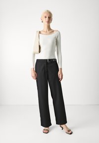 Off-white fitted lange mouwen top met wijde halslijn, gecombineerd met hoge zwarte wijdvallende broek en zwartjes met hakken met bandjesdetail.