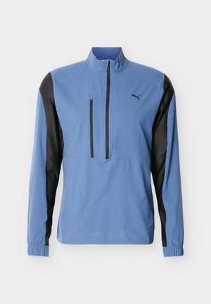 Pulover sport albastru deschis cu mâneci lungi, cu panouri laterale negre, buzunar cu fermoar pe piept, închidere cu fermoar pe jumătate, manșete elastice și logo Puma pe piept.