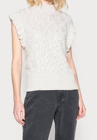 Pull en maille gris clair avec un col montant, un motif texturé et des manches courtes à volants ; associé à un jean foncé.