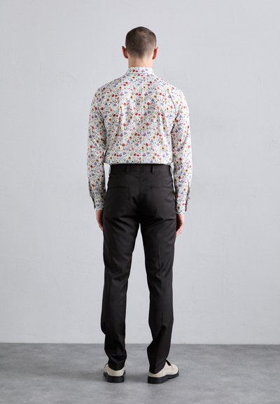 Floral-patterned shirt with multicolored flowers on a white background, paired with black trousers and light-colored shoes.