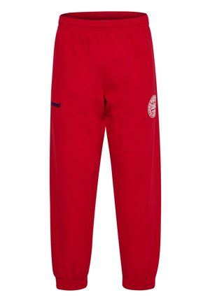 Pantalon de sport rouge avec ceinture élastique et bords-côtes, arborant un logo circulaire blanc sur la cuisse droite et un petit texte noir sur la cuisse gauche.