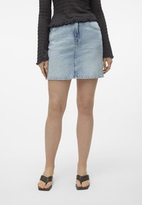 Denim mini kjol i ljusblått med rak passform, framfickor och en subtil blekning. Bärs med en svart texturerad långärmad topp och sandaler.