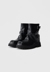 Mustad nahast pahkluukontsaga saapad, millel on voltidega disain, kaks metallist pandlat välimisel küljel ja paks, sooneline tald.