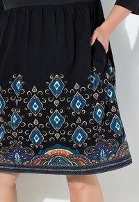Schwarzer Rock mit bunten Paisley- und Diamantmustern. Verfügt über einen gerafften Taillenbund, seitliche Taschen und einen dekorativen Saum. Weiche Stoffstruktur.