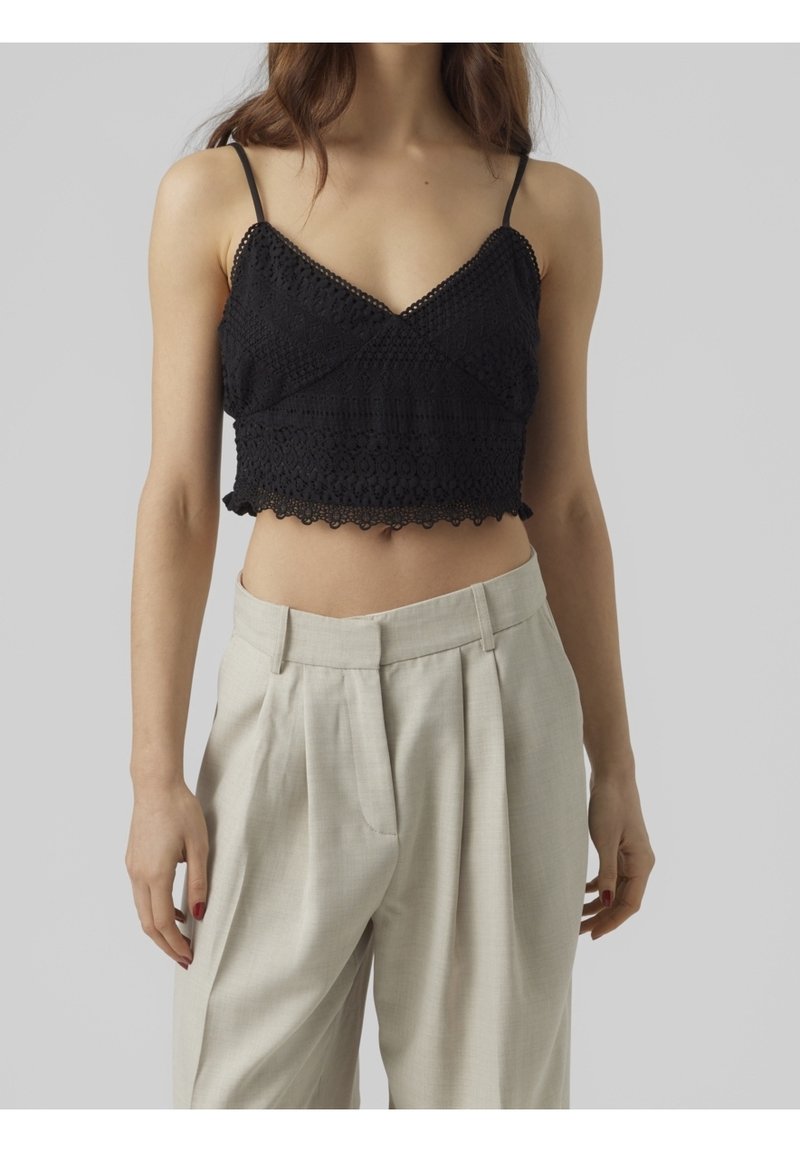 Haut court noir en crochet avec des bretelles fines, doté d'un ourlet festonné et d'un design texturé, associé à un pantalon beige taille haute.