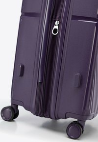 Valigia rigida viola con una superficie liscia, apertura con cerniera e due ruote nere. Presenta maniglie laterali e scanalature verticali sulla superficie.