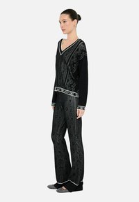 Maglione in maglia nera e pantaloni con un intricato motivo floreale grigio. Presenta un scollo a V, rifiniture a contrasto bianche e una vestibilità a gamba larga.
