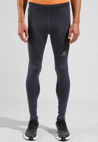 Zwarte sportleggings gemaakt van rekbare stof, met een gladde textuur en een reflecterend logo op de linker dij, gecombineerd met zwarte sneakers.