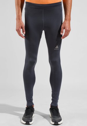 Black athletic leggings made of stretchy fabric, featuring a smooth texture and a reflective logo on the left thigh, paired with black sneakers.