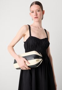 Pochette rayée noir et blanc, de forme arrondie, dotée d'une fermeture éclair élégante. Le matériau semble lisse et brillant.