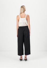 Witte mouwloze top met kantafwerking, gecombineerd met zwarte wijde broek. De outfit heeft een ontspannen pasvorm en een soepele textuur.