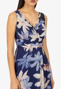 Abito floreale in navy con corpino plissettato, scollatura a V e motivi di fiori pastello. Tessuto morbido con una silhouette fluida, lunghezza al ginocchio.