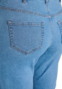 Hellblaue Jeans mit hoher Taille, ausgestattet mit zwei Gesäßtaschen, sichtbaren Nähten und einer glatten Textur.