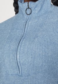 Ljusblå stickad polotröja med hög krage, med en halvdragkedja och ett strukturerat mönster. Mjuk, mysig material med detaljer.