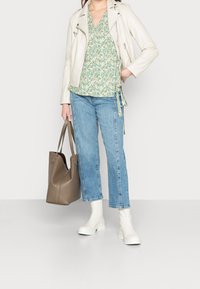 Lichtbeige leren motorjack, groene bloemige wikkelblouse, lichtgewassen rechtlopende jeans, witte enkellaarsjes en een bruine schoudertas.