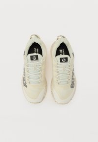 Lys beige sneakers har mesh og syntetiske materialer med en teksturert finish. Detaljene inkluderer "GORE-TEX"-merking og en flekkete såle.