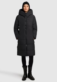 Čierna puffrová bunda s vysokým golierom, celoprepínacím zipsom a veľkými vreckami. Má rovný strih a hladkú, matnú textúru.
