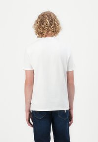 Hvit t-skjorte med korte ermer og rund hals, laget av myk bomull. Bakvisning viser ensfarget stoff, uten mønstre eller grafikk, parret med mørkeblå jeans.