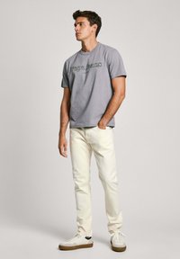 Šedé bavlněné tričko s logem "Pepe Jeans", spárované s bílými džíny a bílými teniskami s hnědými podrážkami. Jednoduchý, neformální vzhled.