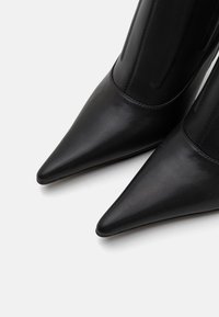 Černé kožené kotníkové boty se špičatou špičkou a elegantním siluetou, s hladkou texturou a minimalistickými designovými prvky.