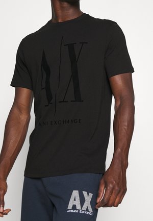 Mand iført sort Armani Exchange t-shirt med stort AX-logo og mørkeblå shorts med hvidt AX Armani Exchange-logo.